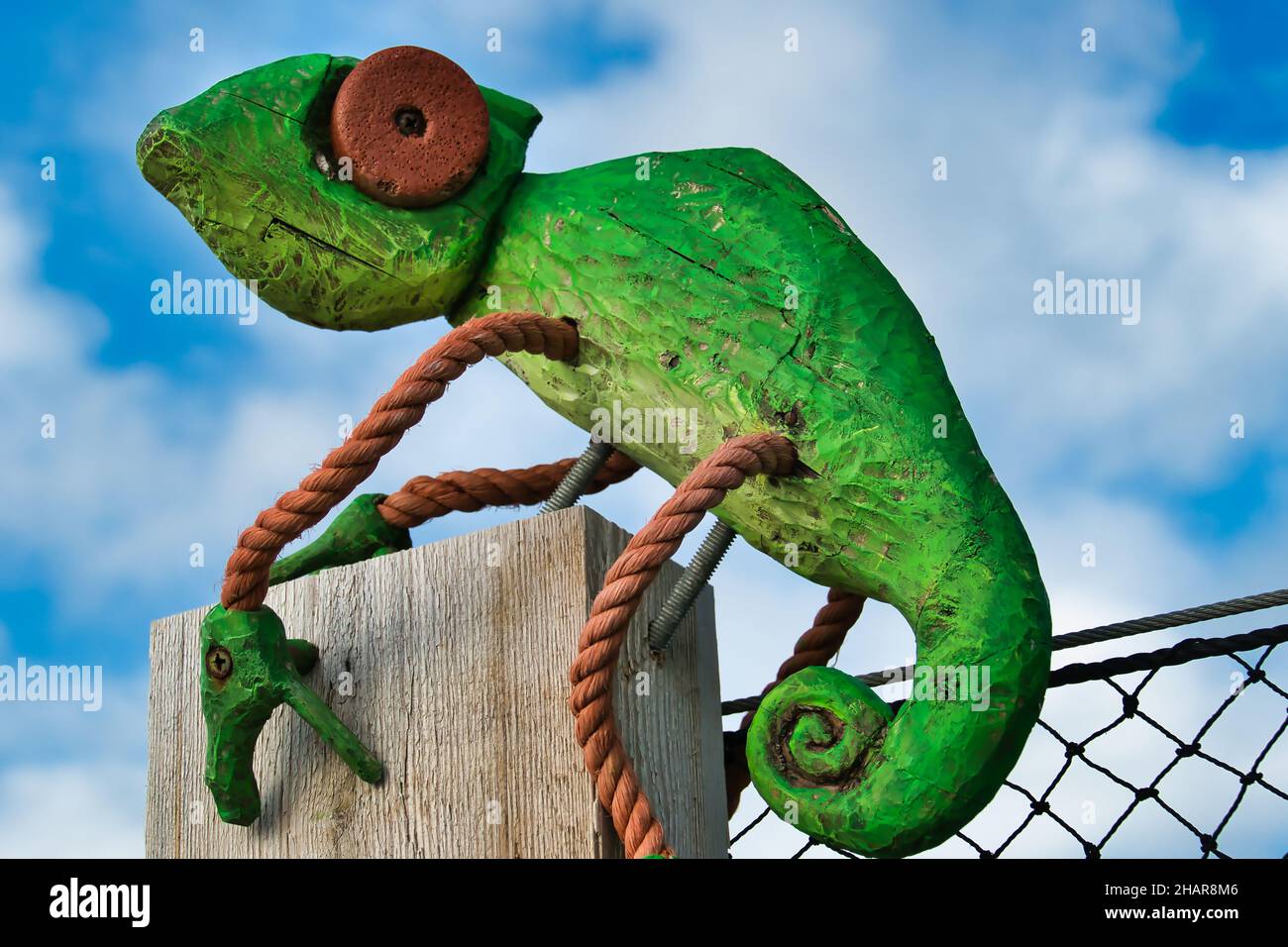Image of a bright green chameleon, made of driftwood and orange rope. Folk art on a fence near Faro, Algarve, Portugal Stock Photo