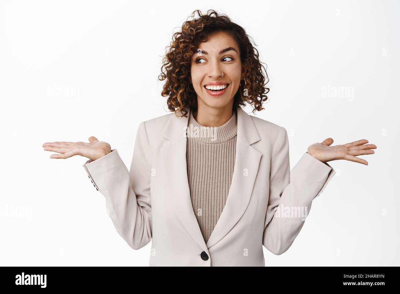 Image of cute corporate woman, office lady shrugging shoulders and smiling, looking unaware, clueless, dont care, standing in suit over white Stock Photo