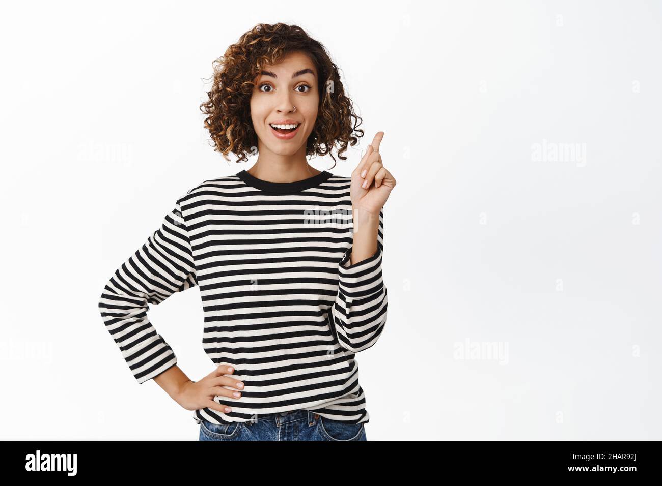 Enthusiastic middle eastern girl pointing finger up, has solution, eureka gesture, suggesting an idea or plan, standing over white background Stock Photo