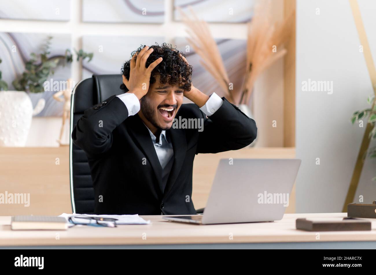 Frustrated young adult ceo, businessman or manager from India, with a  beard, sitting at a table in the office, frustrated with financial losses,  collapse, stressed with hand gestures, shouts Stock Photo -
