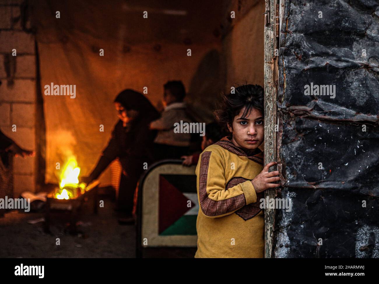 A Palestinian girl looks on as her family sits around a fire to keep ...