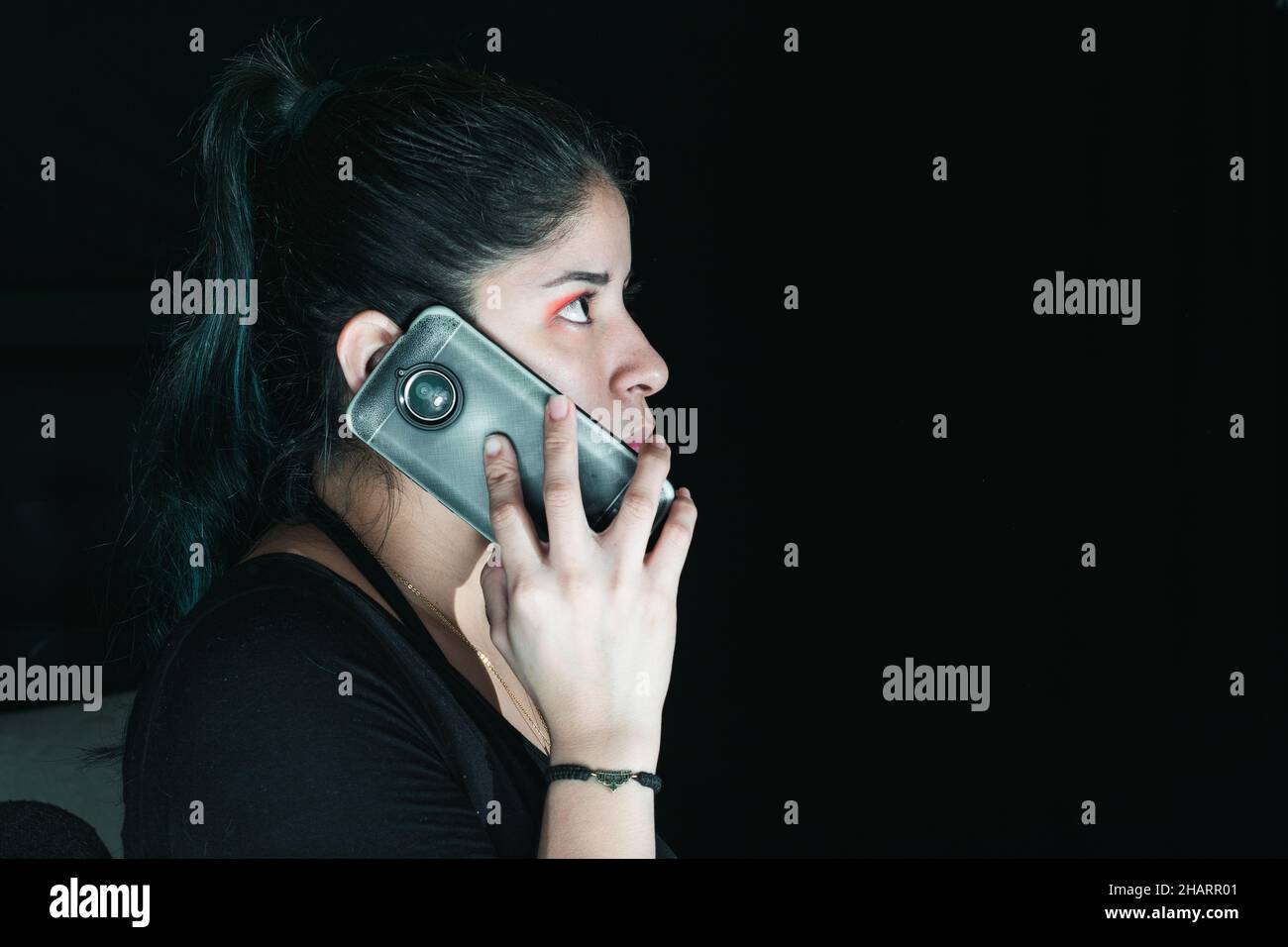beautiful latina woman with green hair receiving an extortion call, with her cell phone in her hand. with her gaze upwards and serious look. with a bl Stock Photo