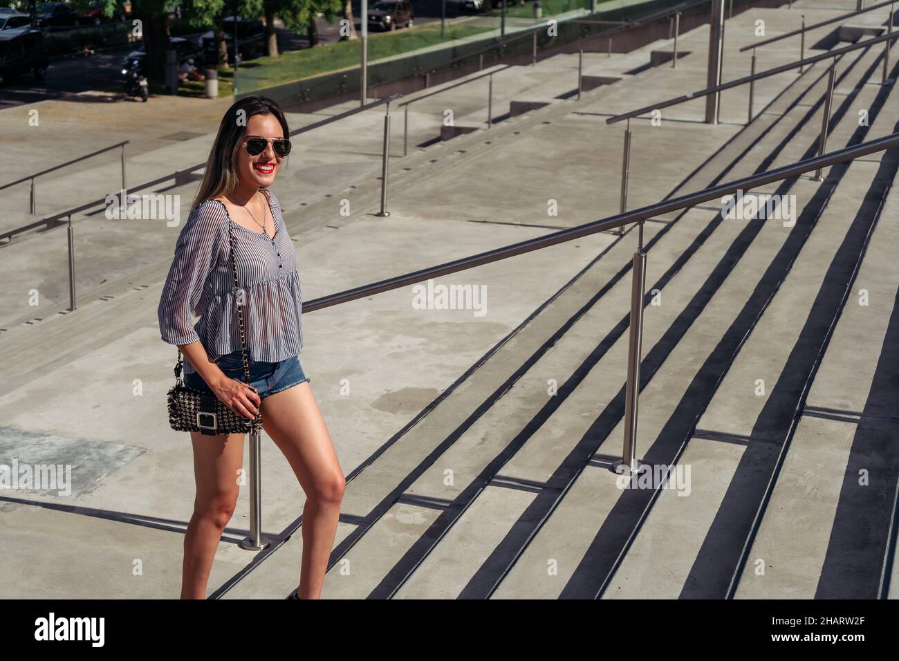 a Full-length shot of a beautiful Latina woman smiling and climbing a concrete staircase on a sunny day. Stock Photo
