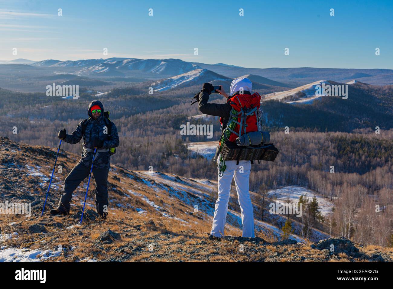 A middle-aged couple go hiking in the alpine winter mountains at dawn - they make a photo with smartphone. Stock Photo