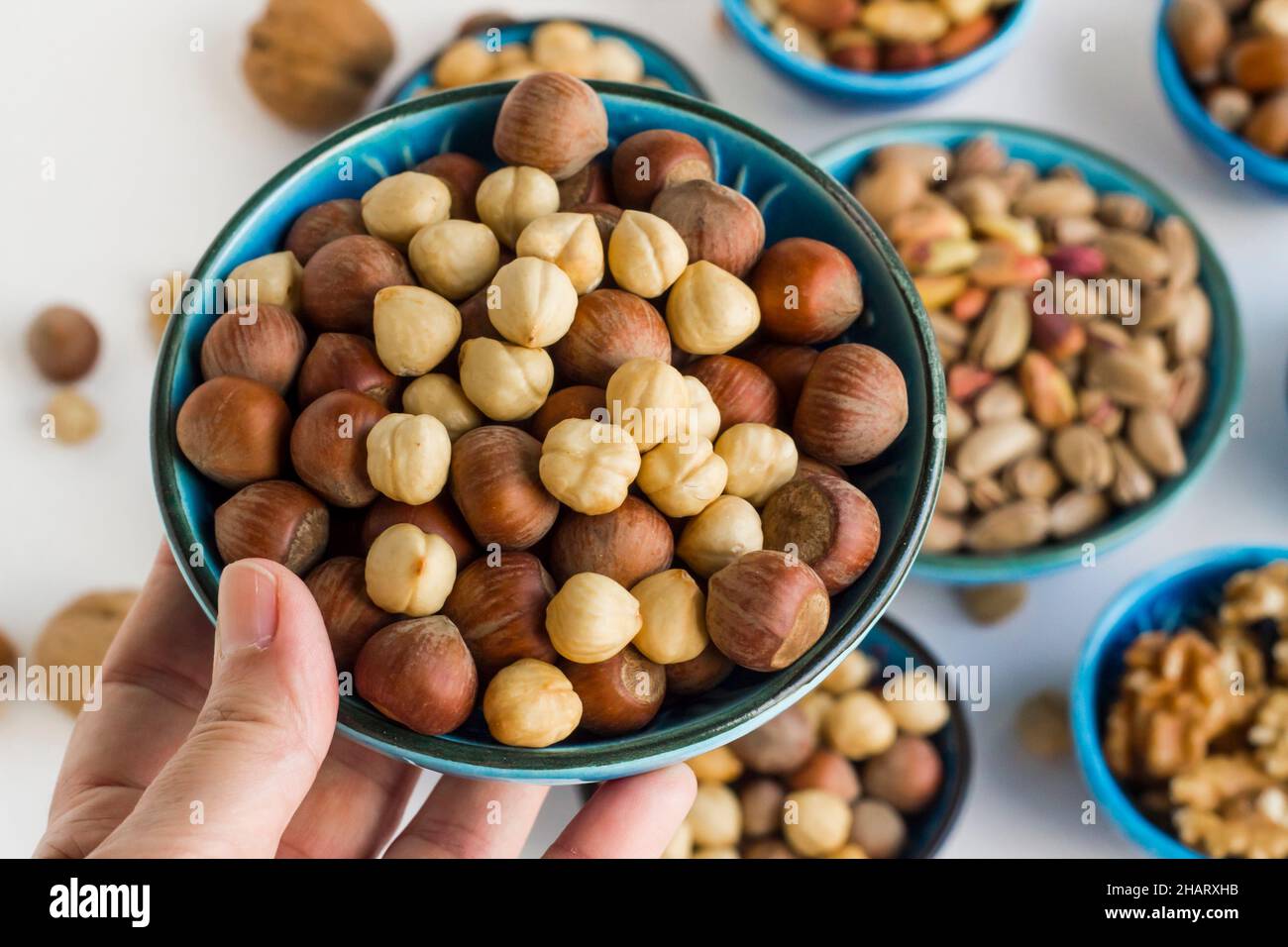 Hand holding a blue ceramic bowl full of nuts aganist other bowls,close up taken Stock Photo