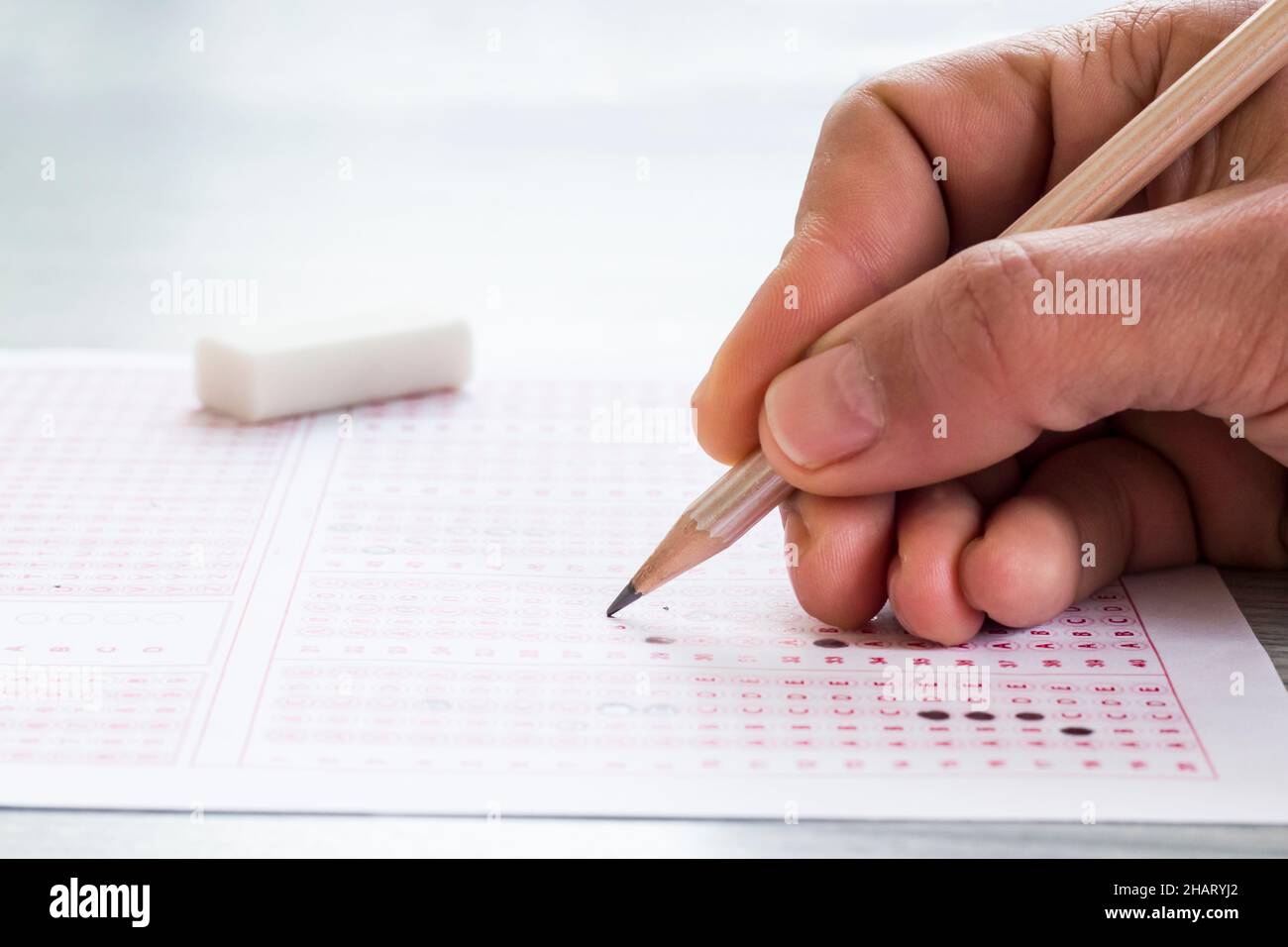 Hand is filling sheet of exam with wooden pencil,conceptual image of education qualifying test exam. Stock Photo