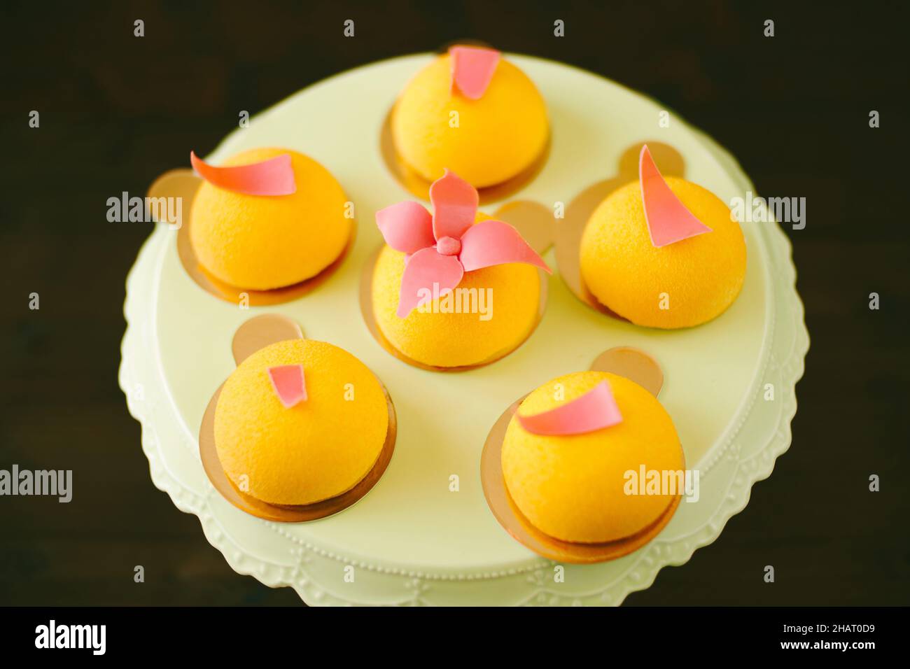 Individual yellow mousse cakes decorated with glazed flowers on an icing turntable Stock Photo