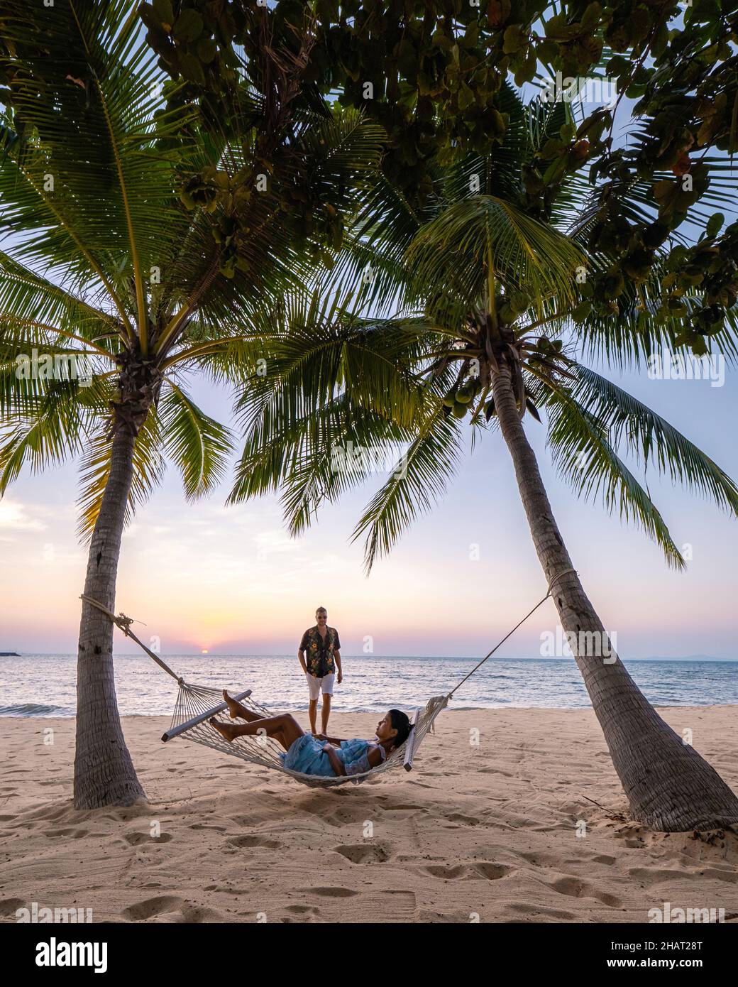 NaJomtien Pattaya Thailand, Hammock on the beach during sunset with palm trees. couple man and woman mid age watching sunset at Na Jomtien Pattaya. Asian woman and European man Stock Photo