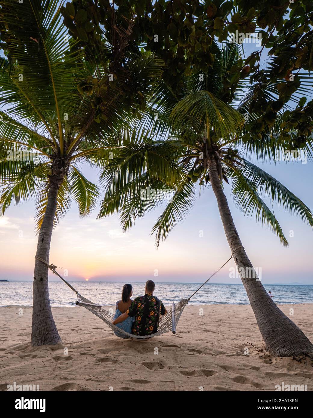 NaJomtien Pattaya Thailand, Hammock on the beach during sunset with palm trees. couple man and woman mid age watching sunset at Na Jomtien Pattaya. Asian woman and European man Stock Photo