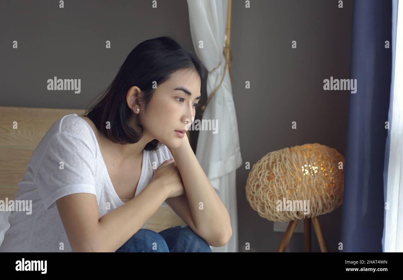 Sad thoughtful young woman pensive face looking away thinking of problems sit alone at home, feels unhappy, lost on unpleasant thoughts, suffering due Stock Photo