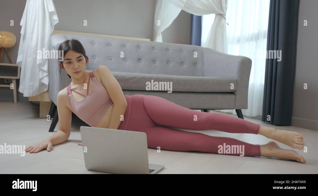 Woman doing side plank at home with online trainer using laptop. Stock Photo