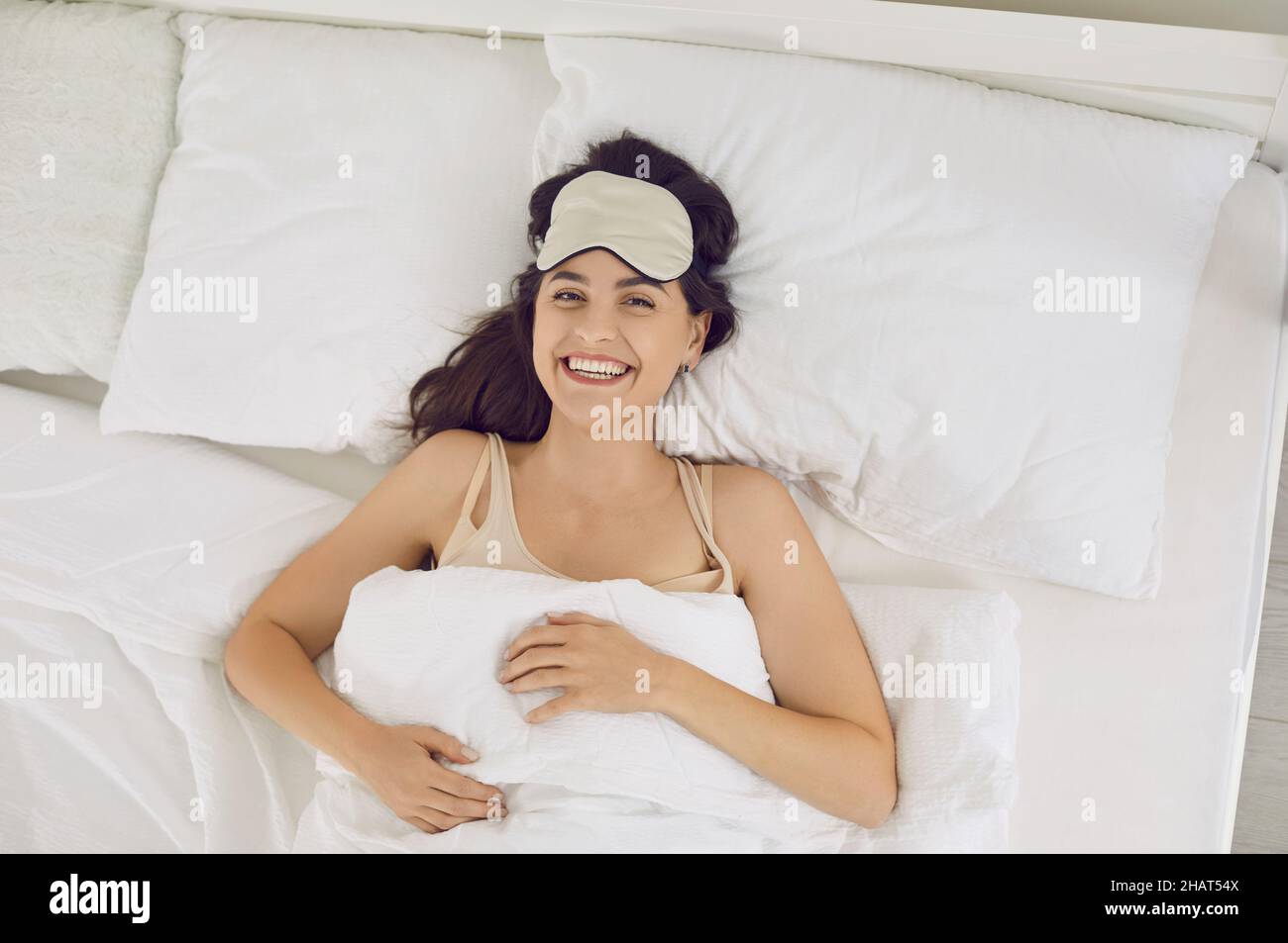 View from above of happy young woman lying in bed after waking up in