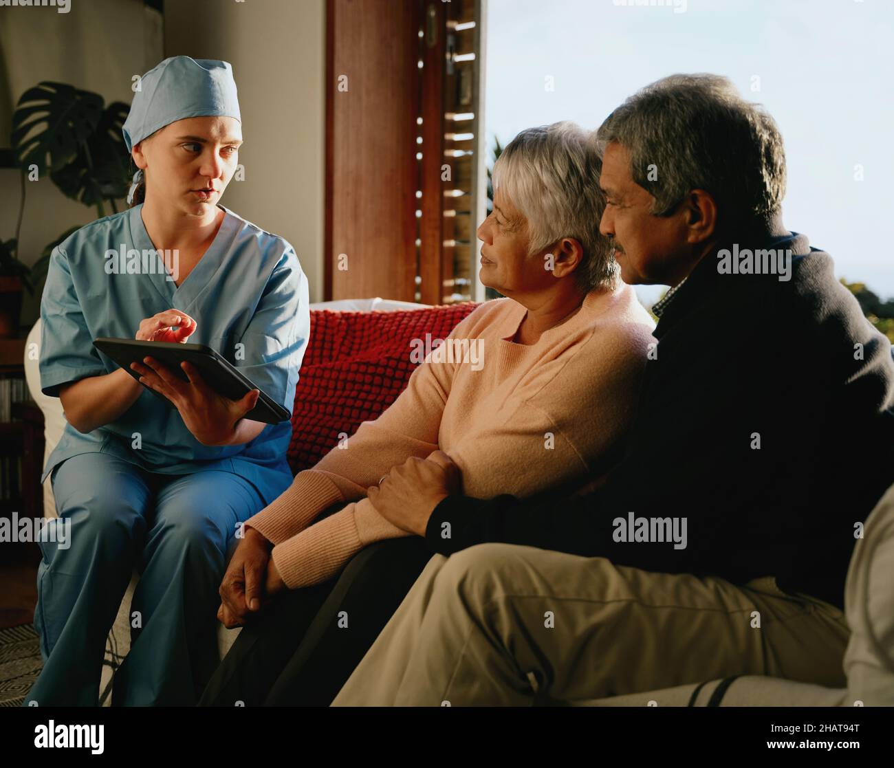 Medical professional explaining negative diagnosis to elderly multi-ethnic couple. Home consultation in modern living room. Stock Photo