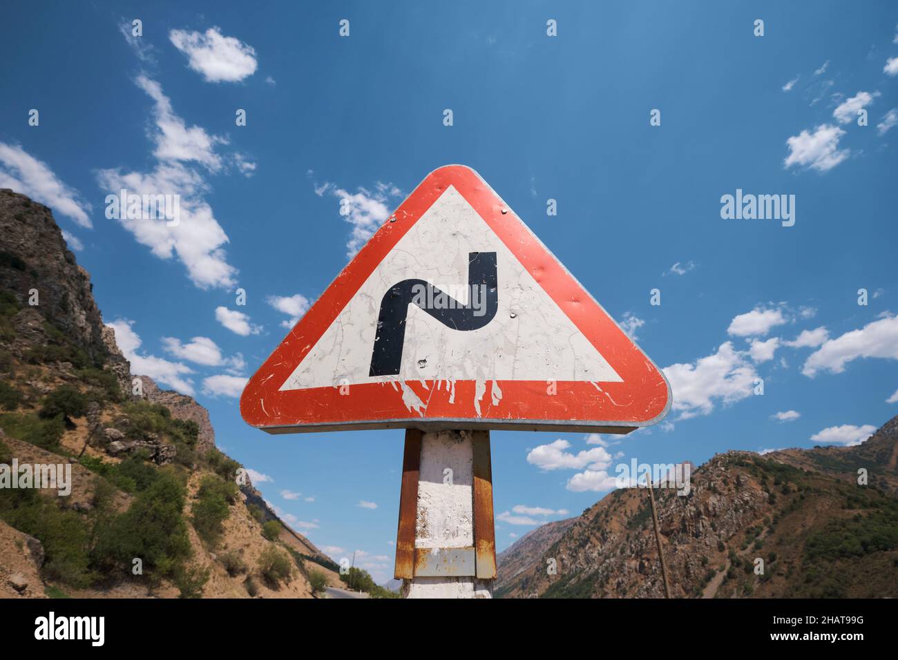 The standard triangle red and white road sign for a curvy section of a road. In the Lake Charvak resevoir area near Tashkent, Uzbekistan. Stock Photo