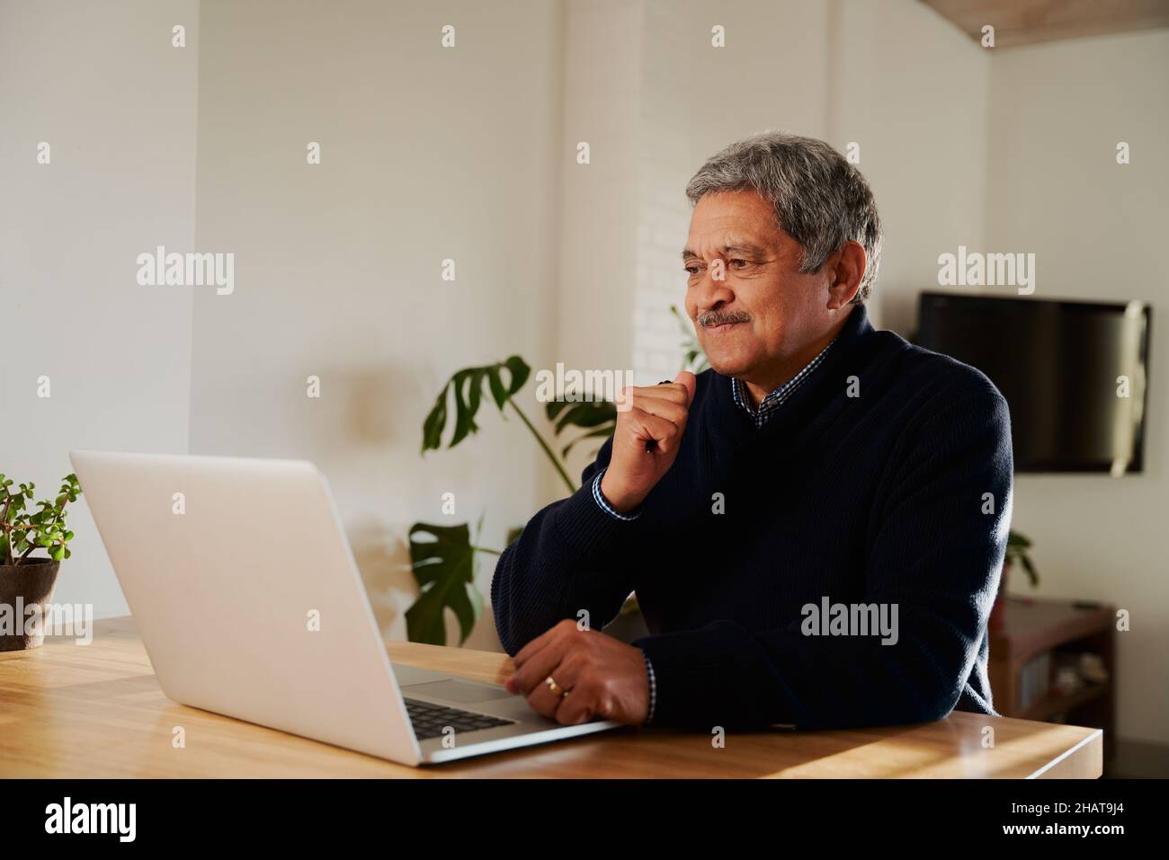 Multi-cultural elderly male frustrated while using laptop. Isolating in modern home, sitting at kitchen counter top. Stock Photo