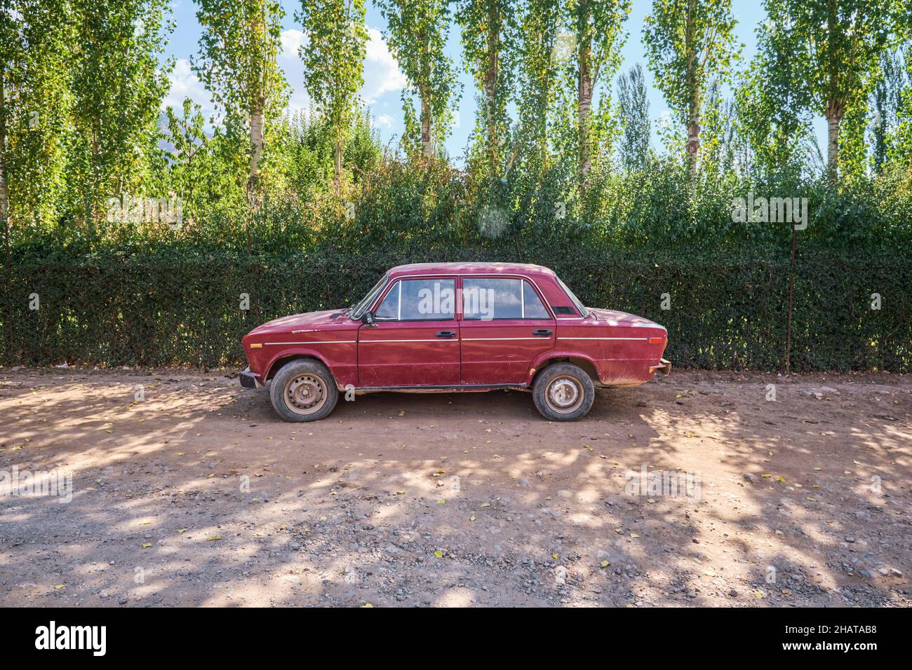 An old, Russian red Lada car parked on a dusty rural road in the country. In the Lake Charvak resevoir area near Tashkent, Uzbekistan. Stock Photo