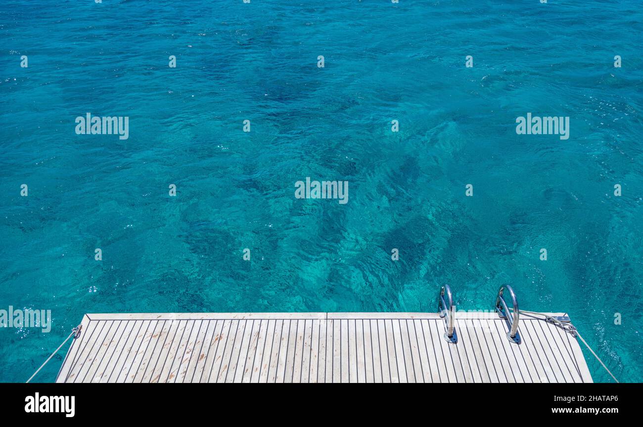 Boat back deck, teak wood and metal ladders, blue sea water background. Luxury yacht cruise, Aegean sea Greece Stock Photo