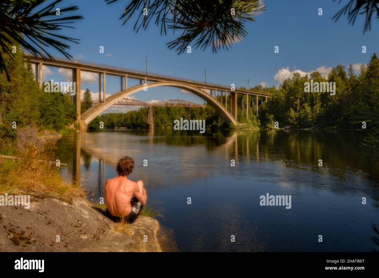 man sitting on roch watching bridges over a river Stock Photo