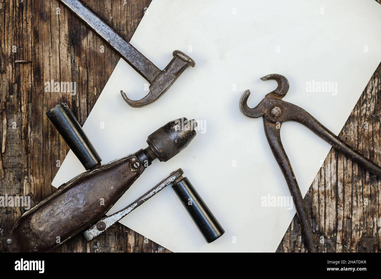 An old hand tool on a cracked wooden surface. Hand drill, hammer and pliers. Top view. Stock Photo