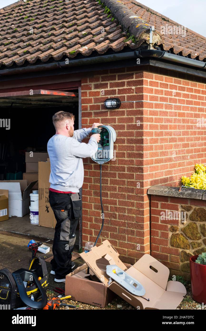 Electrician fitting a Zappi electric car charger to the outside wall of a private garage. NB:  The premises in the photograph are Property Released. Stock Photo