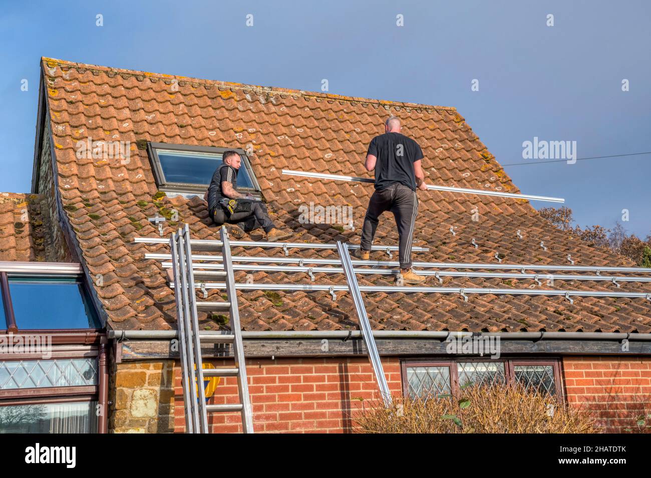 Workers installing solar panels or pv cells on the pantiled roof of a Norfolk cottage.  NB: The premises in the photograph are Property Released. Stock Photo