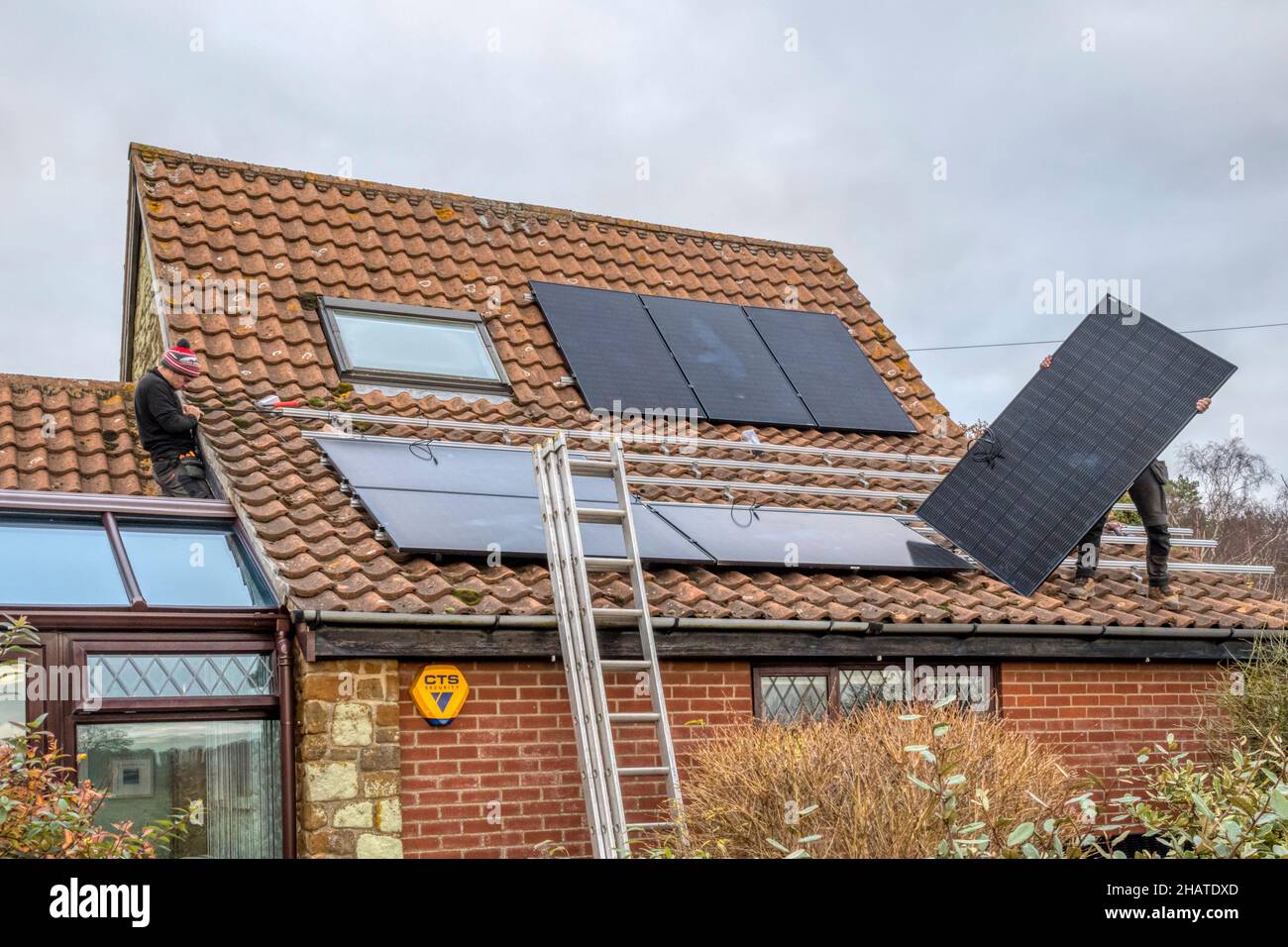 Workers installing solar panels or pv cells on the pantiled roof of a Norfolk cottage.  NB: The premises in the photograph are Property Released. Stock Photo