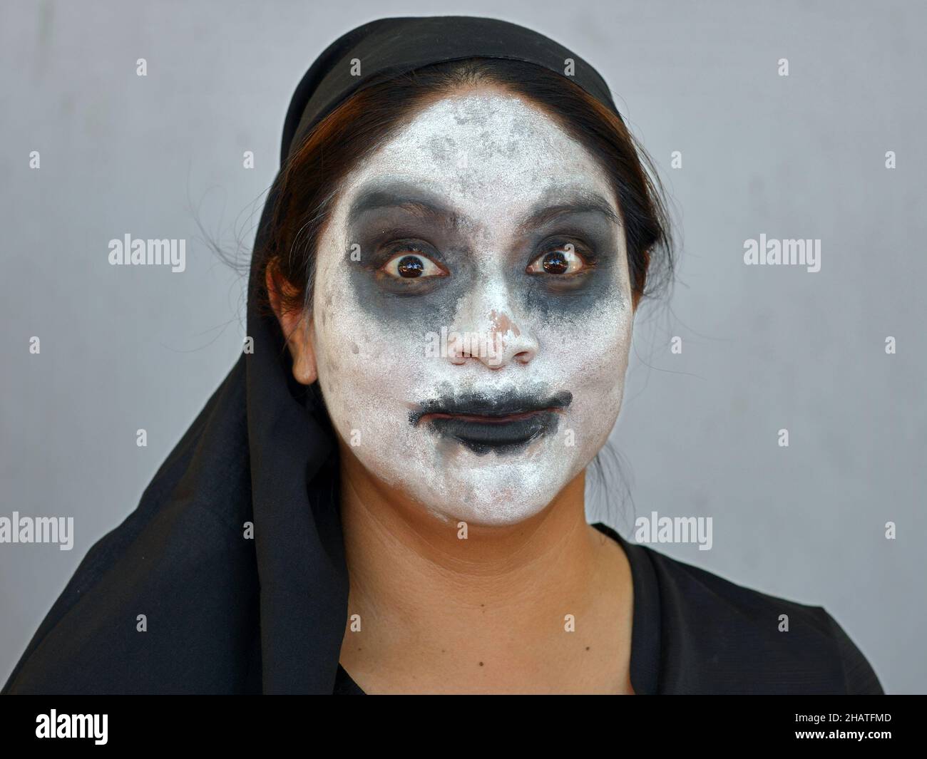 Young Mexican woman with traditional white zombie-like Catrina face make-up on the Day of the Dead (Día de los Muertos) wears black clothes. Stock Photo