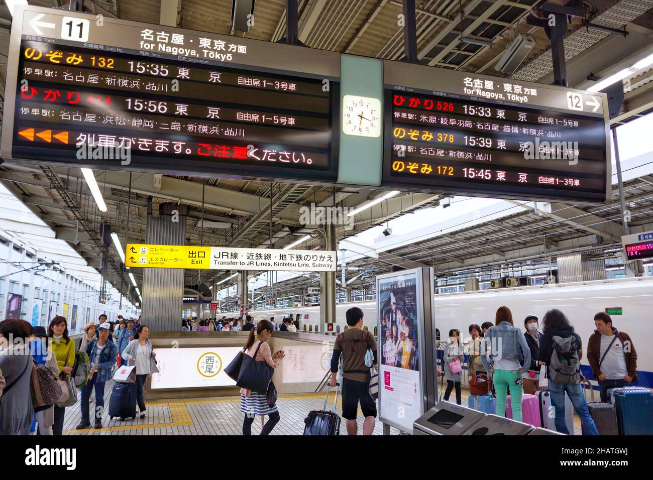Crowd of people waiting on platform at Kyoto railway station with big train schedule information board hanging from ceiling. Stock Photo