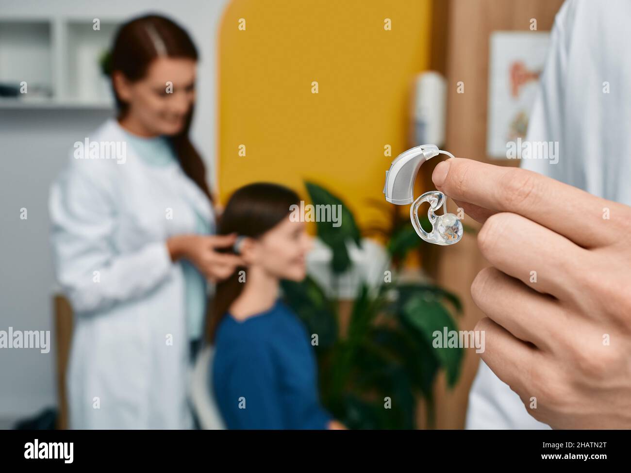 Modern BTE hearing aid in doctor hand, close-up over background audiologist consultation. Selection of hearing aids at audiology clinic Stock Photo