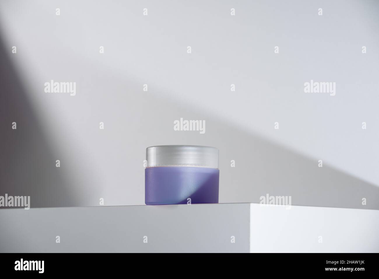 purple cream pot with silver lid on white podium and background. Modern geometric minimalism in self-care beauty. Hero shot Stock Photo