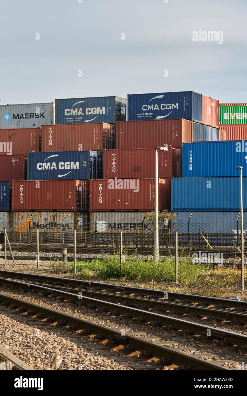 A large pile of shipping containers by rail tracks leading out of Port of Felixstowe central rail freight terminal. Stock Photo