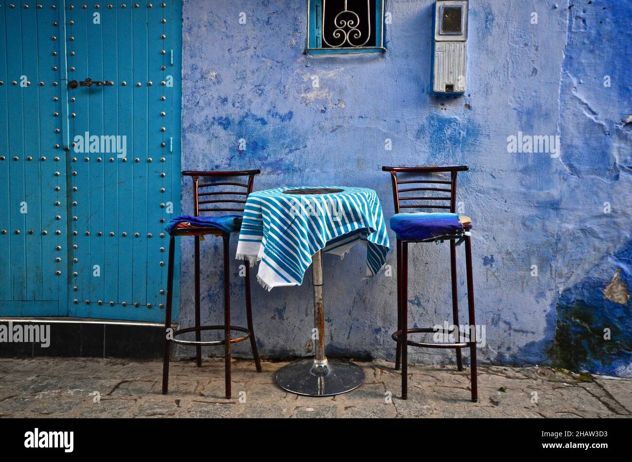 Alley with bar table and two high chairs, blue alley with house entrance, Chefchaouen, Tangier-Tetouan-Al Hoceima, Morocco Stock Photo