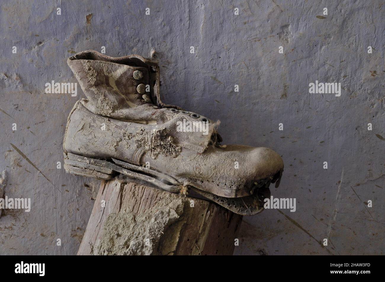 Work shoe with detached sole on wooden trestle in front of grey wall, laceup boots with earth