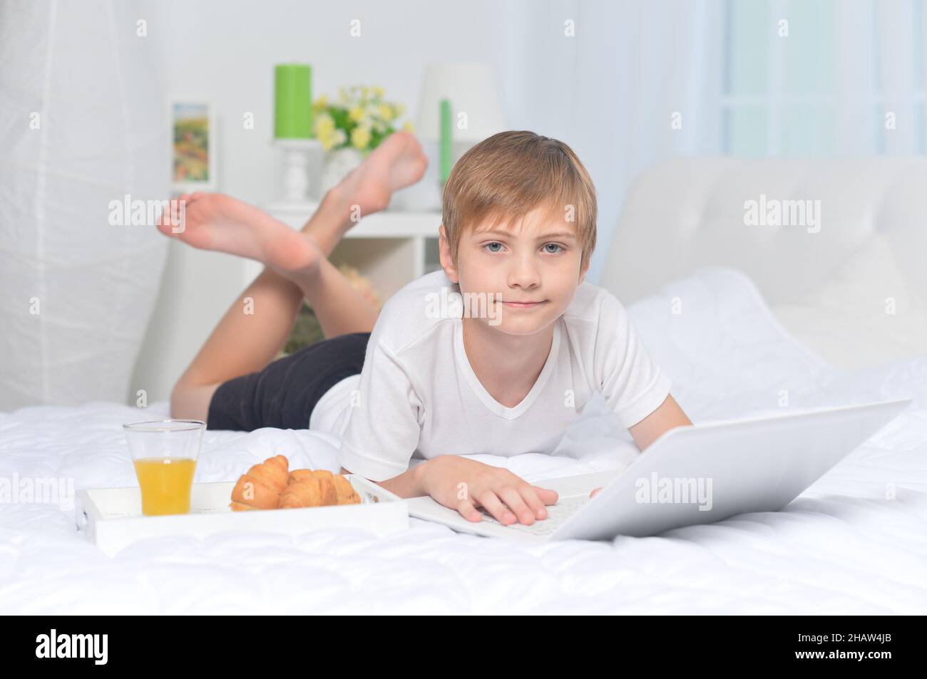 Boy using laptop on bed while having breakfast Stock Photo - Alamy