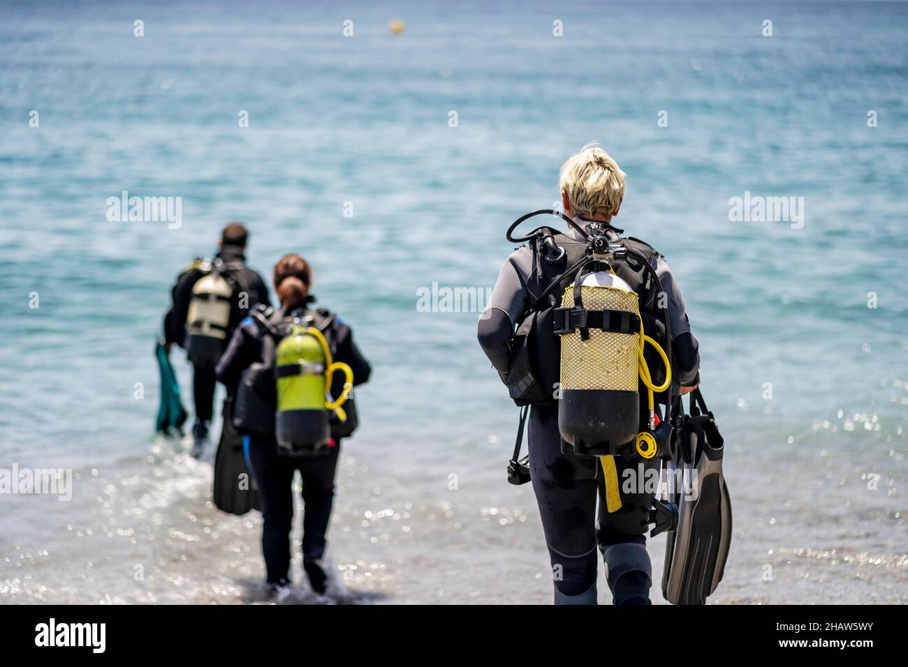 Three scuba divers with all equipment heading to the sea, Andalusia, Spain Stock Photo
