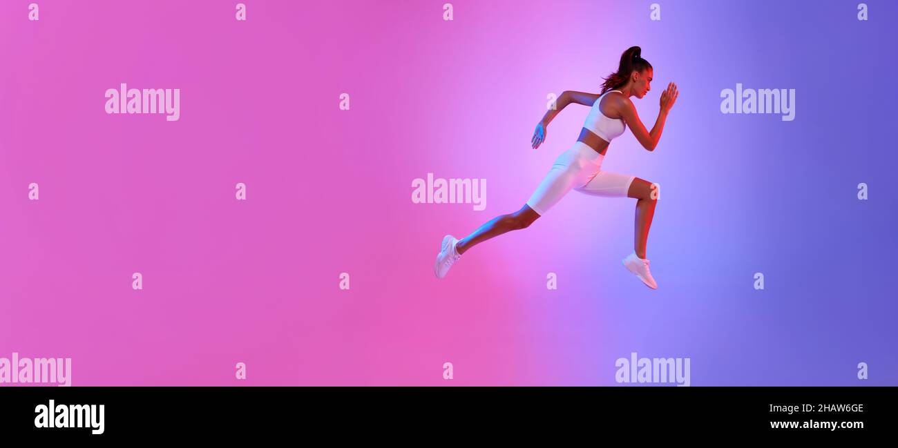 Sporty Female Running In Mid-Air Exercising Over Neon Background, Panorama Stock Photo