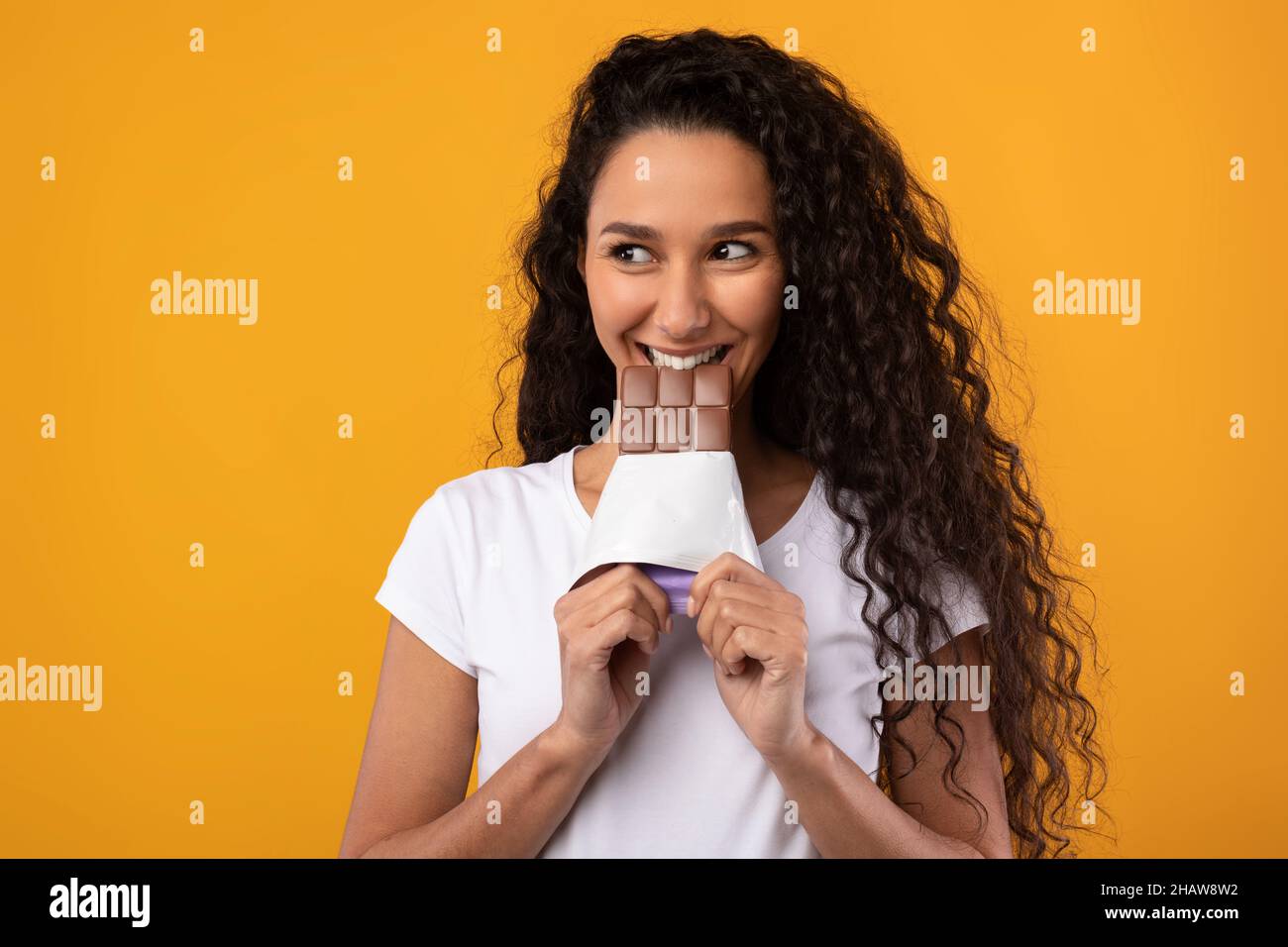 Funny Latin Lady Holding And Biting Chocolate At Studio Stock Photo