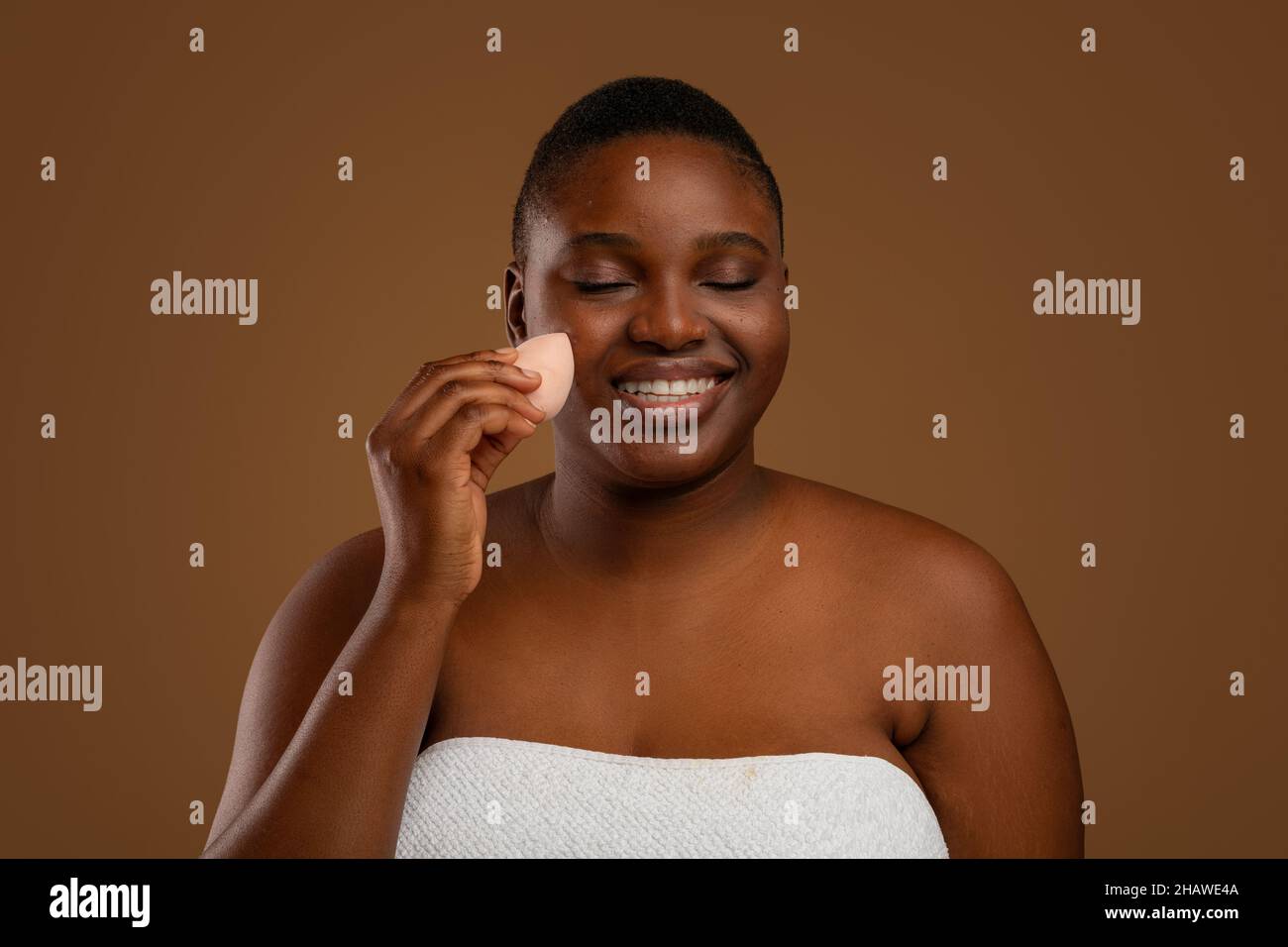 Black chubby woman with acne applying makeup with sponge Stock Photo