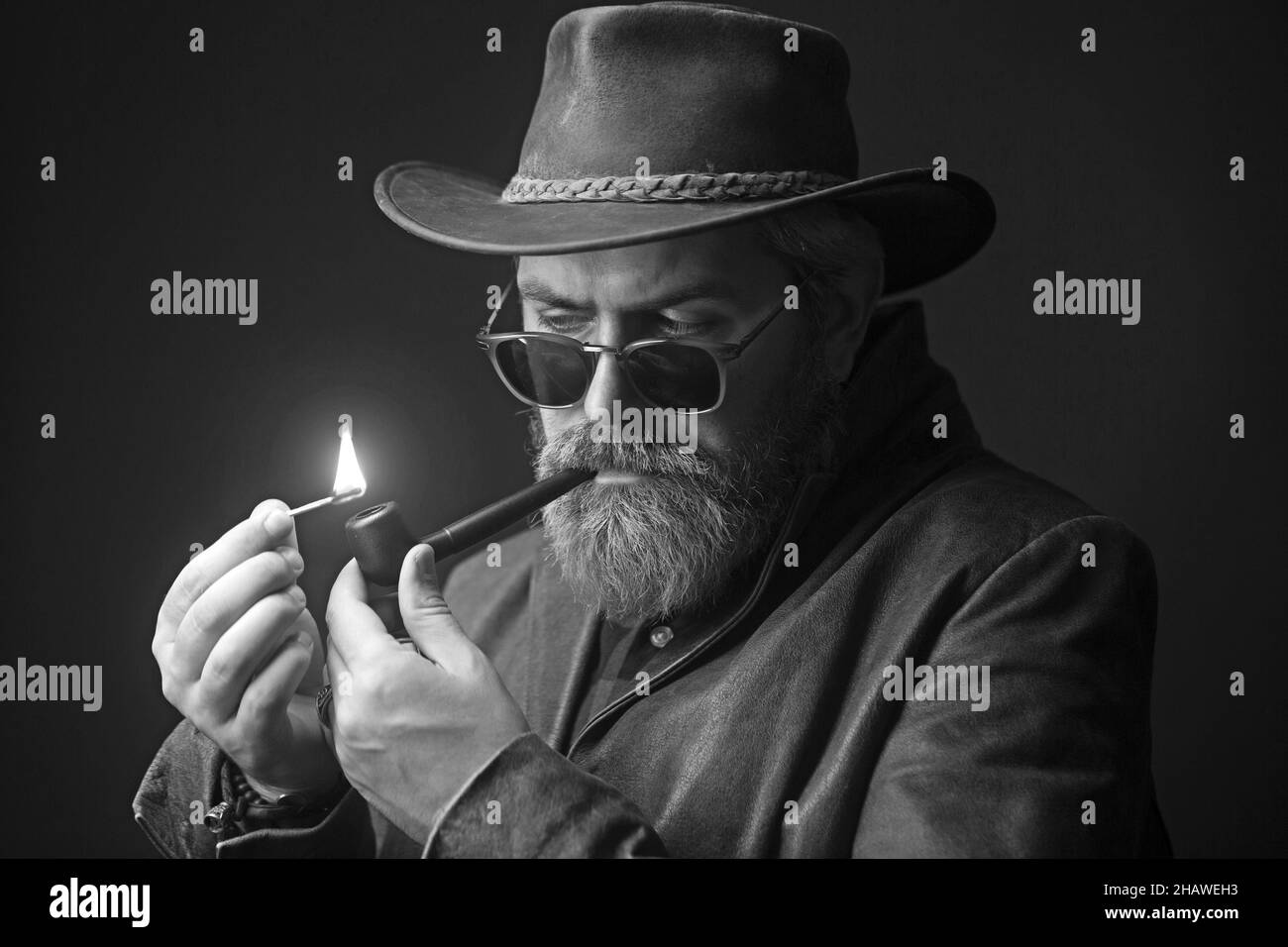 Cool cowboy in leather Jacket with pipe over dark background. Stock Photo