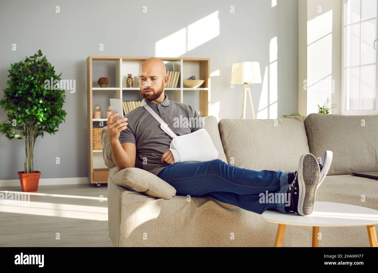 Young patient with broken arm sitting on couch at home and using his