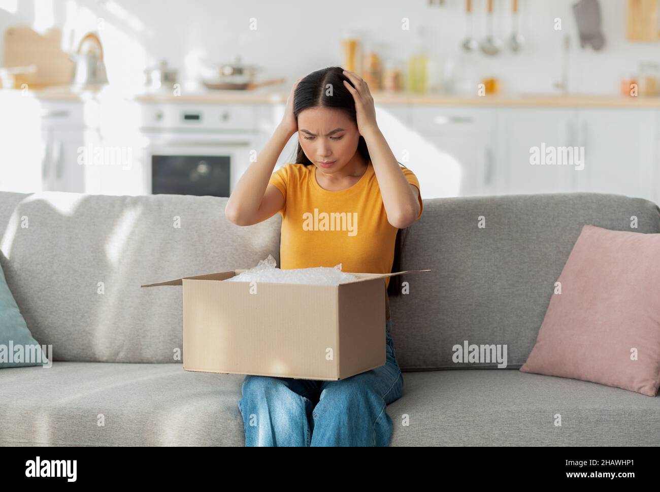 Bad delivery service. Dissatisfied asian lady sitting on sofa with
