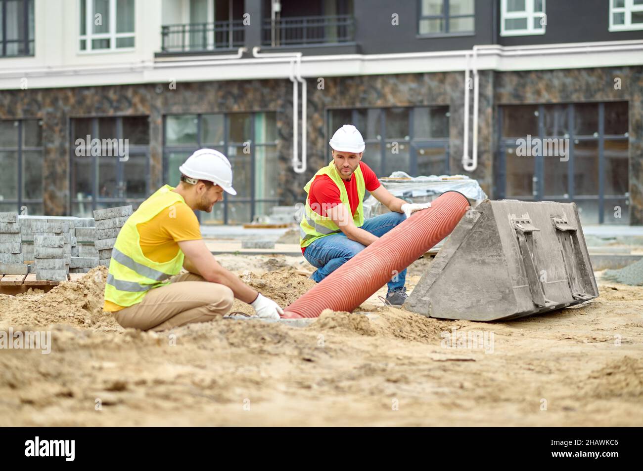Two men crouched near pipe at construction site Stock Photo