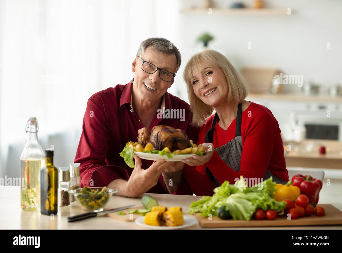 Portrait of happy senior couple holding dish with tasty roasted turkey for family Christmas celebration at kitchen Stock Photo