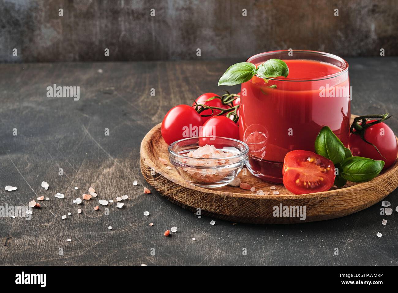 Glass of fresh tomato juice, salt, basil and tomatoes on  wooden stand  on old wooden background. With copy space. Stock Photo