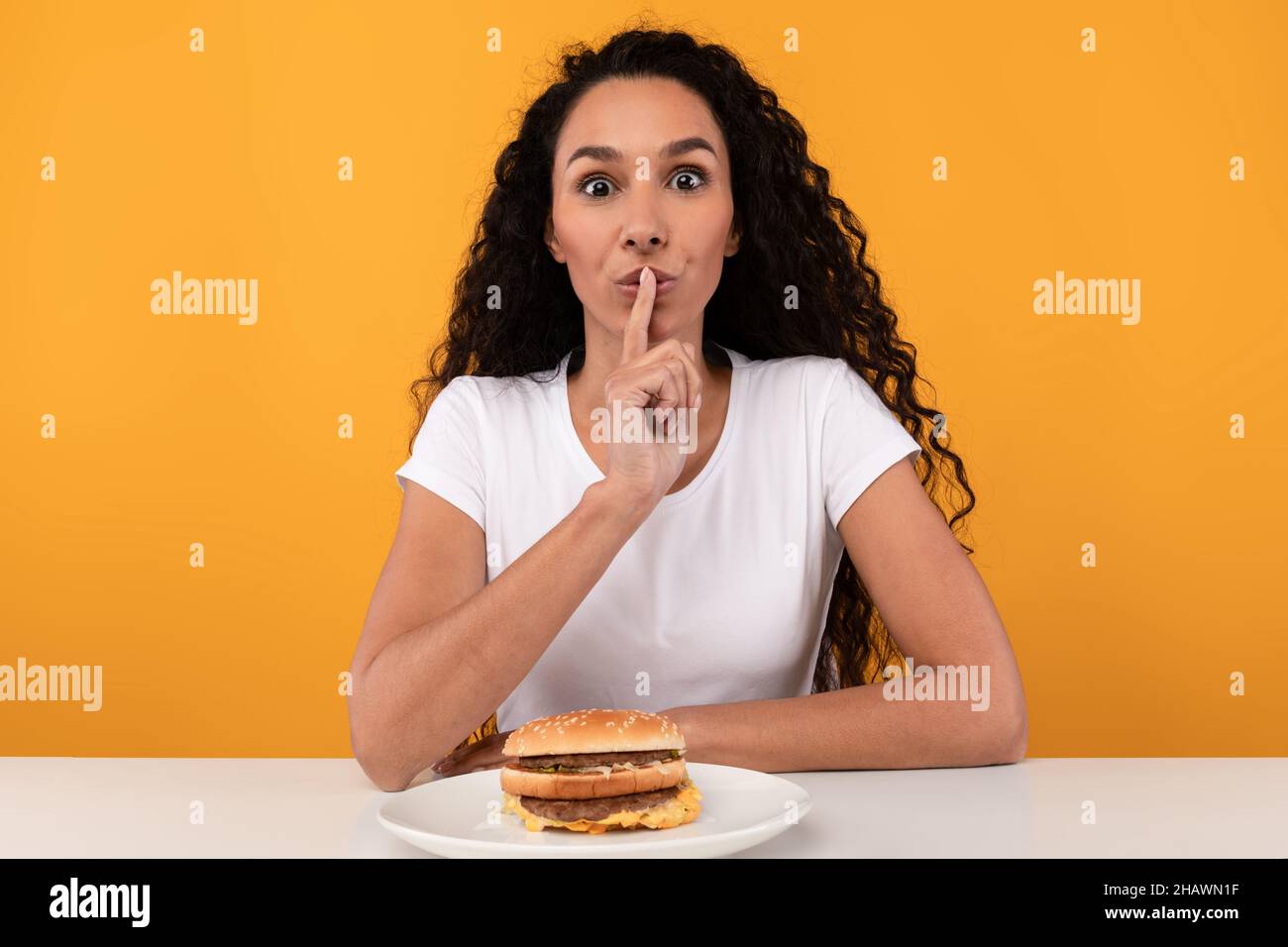 Hungry Lady Showing Silence Gesture Eating Burger Stock Photo
