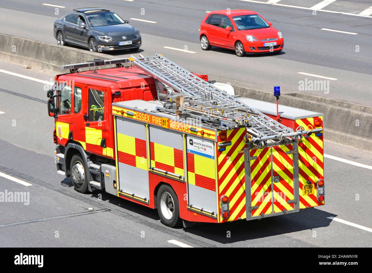 Aerial side back view Essex Fire & Rescue Service fire brigade engine blue light emergency shout driving on UK motorway beside concrete crash barrier Stock Photo