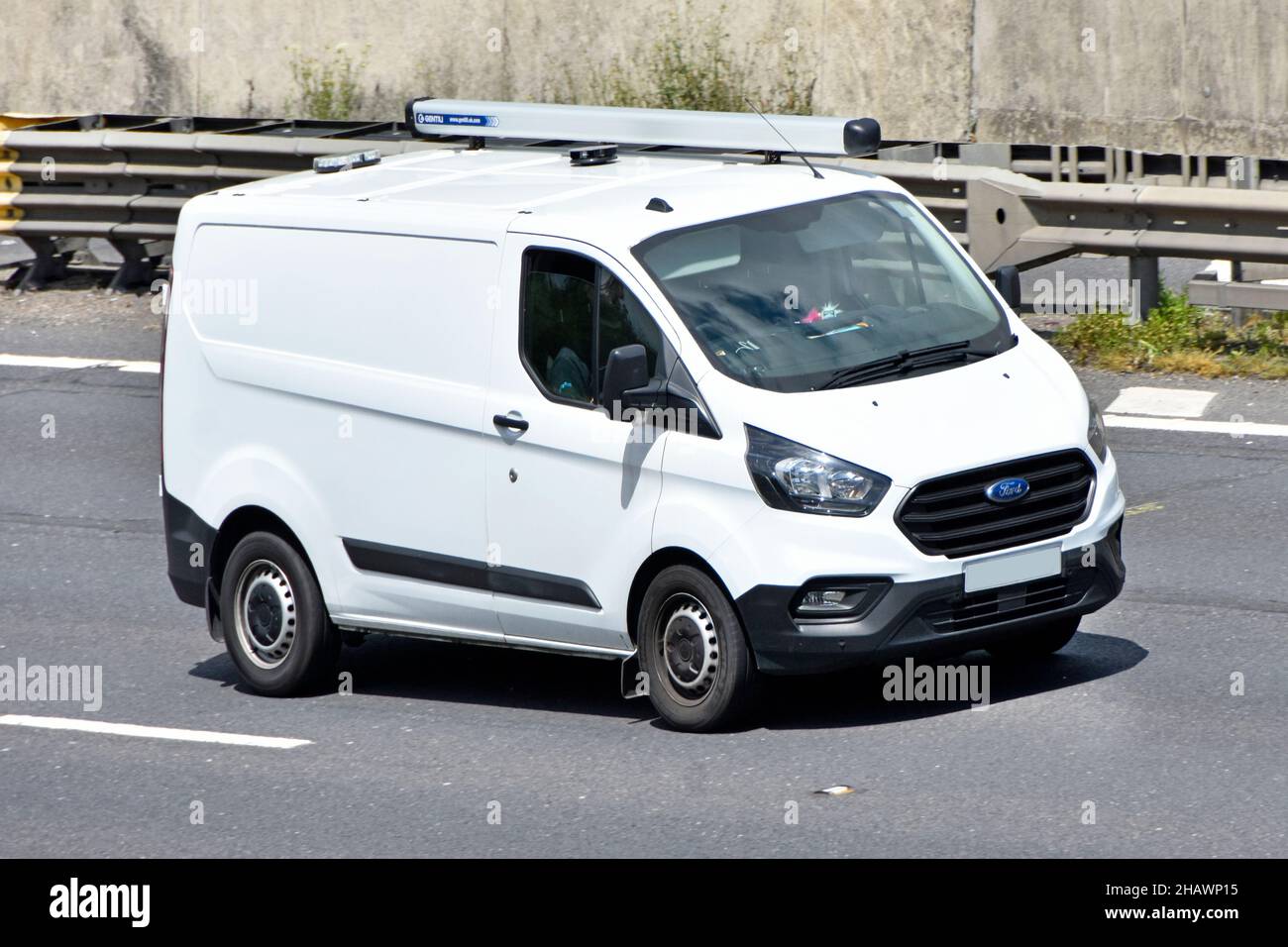 Ford Transit white van & driver close up side front view clean unmarked vehicle fitted roof mounted tubular storage rack driving  on UK motorway road Stock Photo