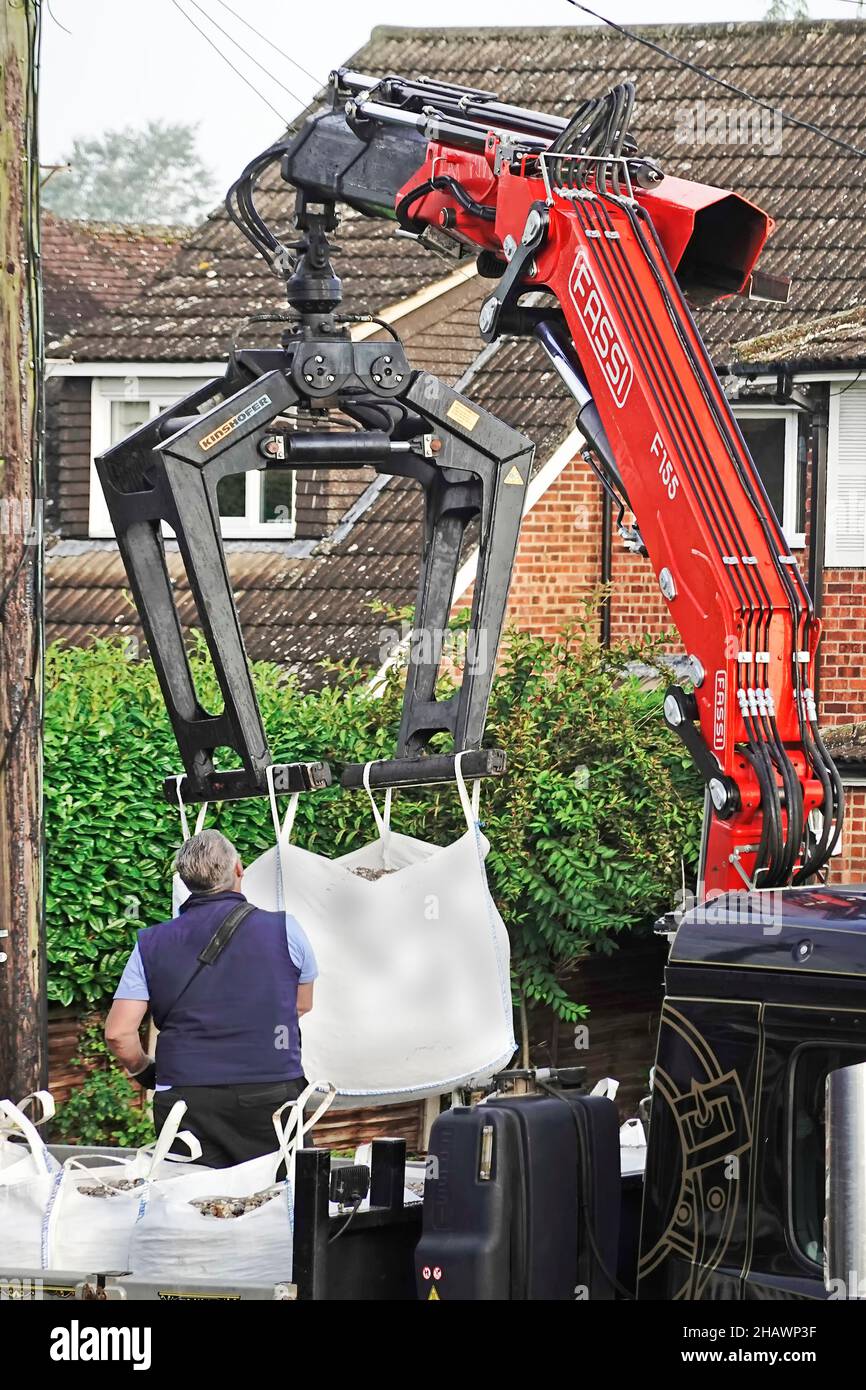 Street scene close up builders merchant lorry mounted hydraulic crane delivery driver lifts jumbo bag building construction site materials England UK Stock Photo