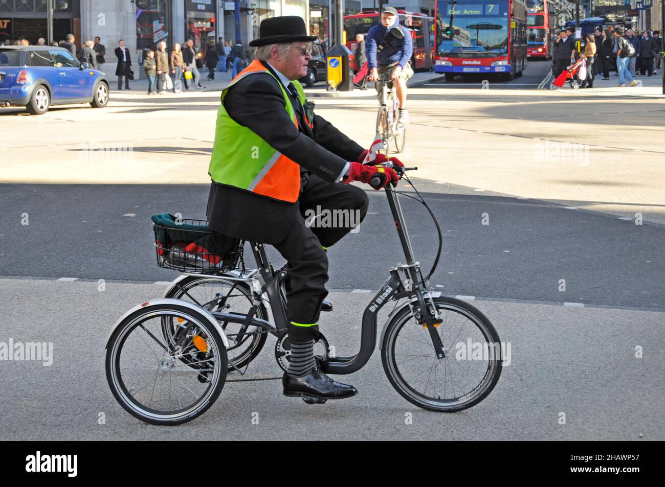 Side view city gent bowler hat wearing high visibility jacket & office suit riding Di Blasi tricycle at Oxford Circus road junction London England UK Stock Photo