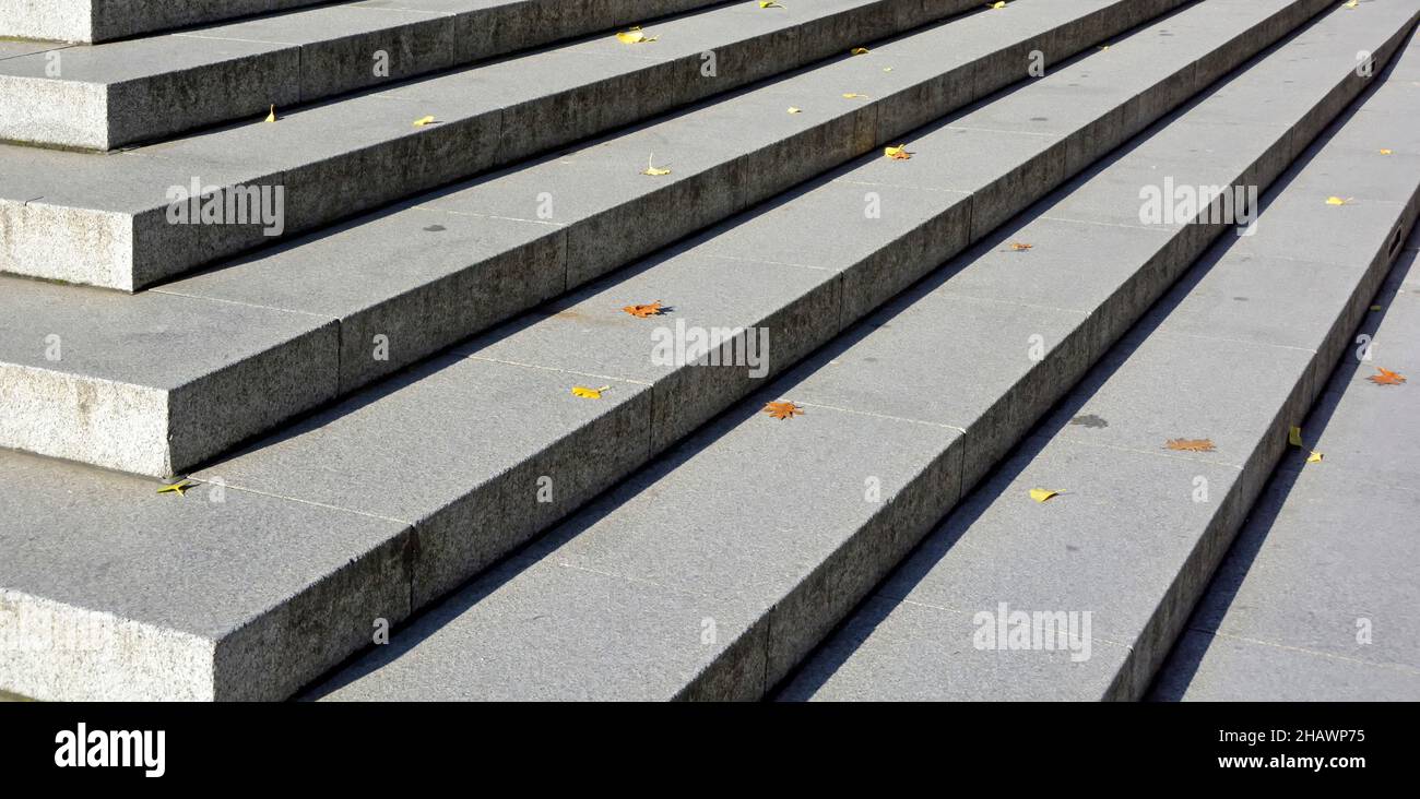 Close up straight line of wide stone treads in sunshine risers in shadow on corner steps in the City of Londonwith fallen autumn leaves England UK Stock Photo